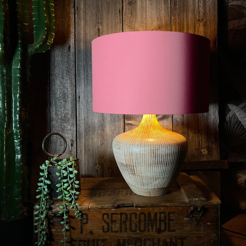 Handcrafted pink cotton lampshade emits soft, warm glow on a table lamp.