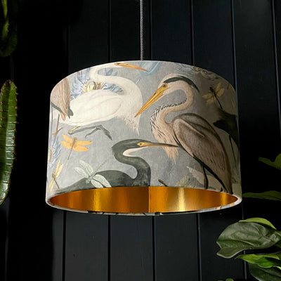 Heron lampshade with blue, grey and fawn-coloured feathers on soft grey velvet fabric, lined with metallic gold.